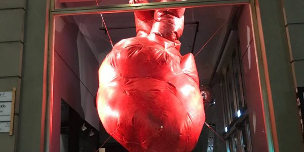 In einem Schaufenster hängt ein großes rotes aufgeblasenes Herz mit mehreren Schnüren gespannt.