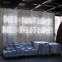 An der Wand eines Holzcontainers stehen in abstrakter Leuchtschrift die Worte „no nature, no future“. Drunter sind Papiere und Platten gestapelt.