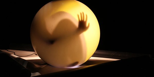 Eine gelbe runde Kugel, in der der Schatten einer Hand zu sehen ist.