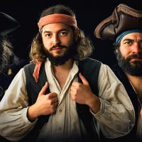 Drei Piraten mit einem Totenkopfschädel und einem Papagei schauen direkt in die Kamera.