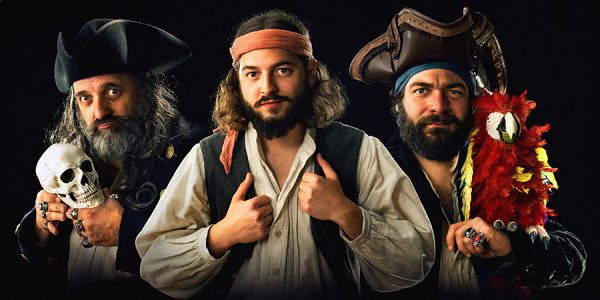 Drei Piraten mit einem Totenkopfschädel und einem Papagei schauen direkt in die Kamera.